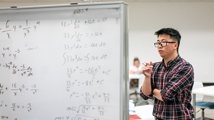 a graduate  student writes an equation on a whiteboard